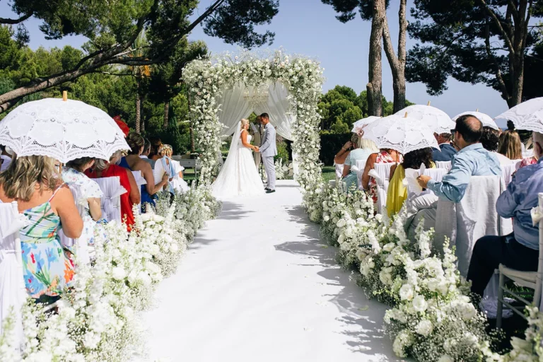 Event Planner: Tracy Lavin Events. Wedding ceremony, white floral arrangement aisle, white umbrellas for wedding guests.