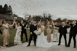 Image of a bride and groom celebrating with confetti amidst friends at a boho wedding in black, gold, and white color scheme.